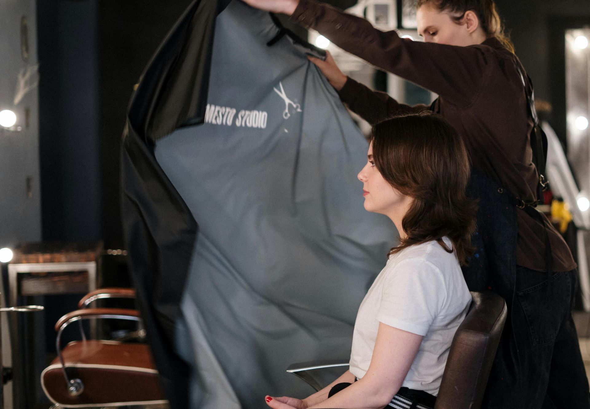 Hair stylist draping cape over client for a haircut in a modern hair salon setting.