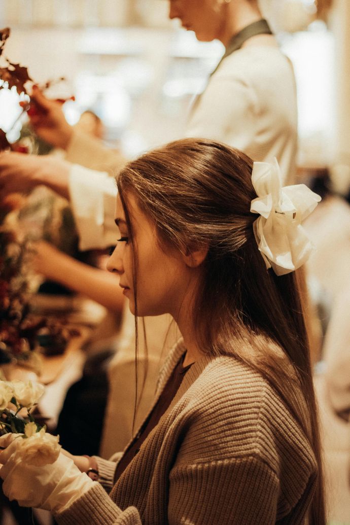Young woman with hair bow arranging flowers at a floral workshop indoors.