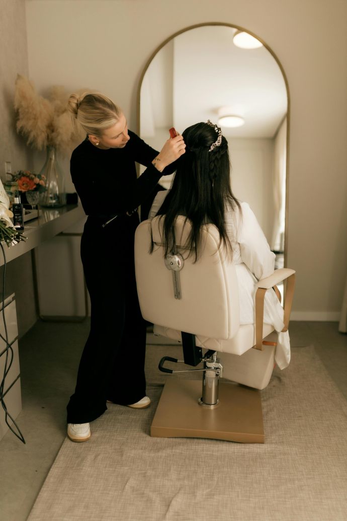 A hairstylist adorns a bride's hair with floral accessories in a chic salon setting.